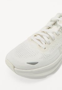 Białe buty sportowe z siateczkową cholewką, teksturowanym wzorem, płaskimi sznurowadłami, amortyzowaną podeszwą i subtelnym szarym logo.