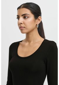 Black long-sleeve top with a scoop neckline. Smooth cotton fabric, fitted design, paired with silver hoop earrings. Light background.