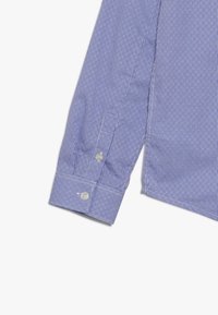 Blå och vit rutad skjorta med långa ärmar, knäppningar vid ärmsluten och rak nederkant. Tillverkad av vävt material med en slät textur.