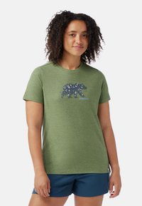 Groene T-shirt met korte mouwen van zachte stof, met een beerafbeelding bedekt met bloemmotieven. Gecombineerd met blauwe shorts.