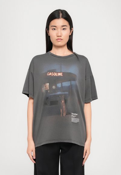 T-shirt grigia oversize con stampa grafica di una stazione di servizio con un cane, bordi sfilacciati e dettagli del logo stampati sull'orlo.