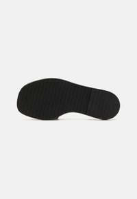 Semelle d'une chaussure noire avec un motif texturé comprenant des formes circulaires entrelacées répétées sur un fond clair uni.