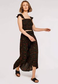 Top court noir à fleurs avec des bretelles volantes, associé à une longue jupe noire fluide dotée d'un motif floral multicolore et d'une coupe décontractée.