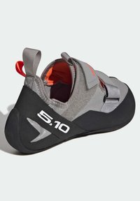 Sapatilha de escalada cinza com sola de borracha preta, tira de velcro e acento vermelho. Apresenta um cabedal texturizado e um logótipo distintivo da 5.10 em branco.