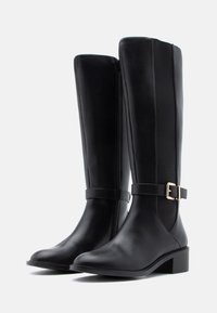 Botas pretas até ao joelho feitas de couro liso, com um fecho lateral, um detalhe de fivela no tornozelo e um salto baixo em bloco.