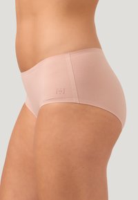 Ljusrosa hipsterunderkläder gjorda av mjukt material, med en sömlös design och varumärkesloggan subtilt präglad på sidan.