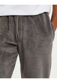 Pantalons de jogging en molleton gris avec une taille élastique, un cordon de serrage ajustable et des poches latérales, dotés d'une surface douce et texturée.
