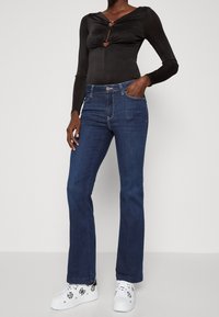 Mustat pitkähihainen body, jossa on sydämenmuotoinen aukko, paritettuna tummansinisiin leveisiin farkkuihin ja valkoisiin tennareihin, joissa on mustia kuvioita.