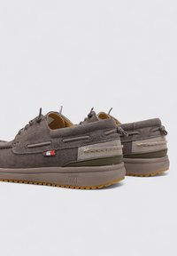 Scarpe in suede marrone con suola piatta, dettagli testurizzati e cuciture sottili. Le caratteristiche includono una suola in gomma antiscivolo e un'etichetta con il logo sul lato.