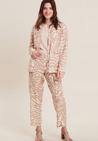 Beige- und weiße Zebra-Print-Jacke und -Hosen-Set mit lässiger Passform. Die glatte Stofftextur und große Taschen sind sichtbar.