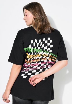 Zwarte oversized t-shirt met kleurrijke tekst "ALLES WAT JE WIL" in verschillende lettertypen op een geruit patroon aan de achterkant.