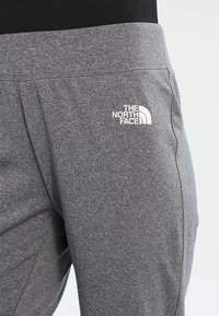 Szare spodnie dresowe wykonane z miękkiego materiału, o gładkiej fakturze i białym logo "The North Face" na lewej nogawce.