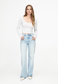 Un cropped top gri deschis cu mânecă lungă, asociat cu blugi evazați de un albastru deschis. Ținuta are o textură netedă și un design minimalist. Pantofi cu vârful ascuțit.