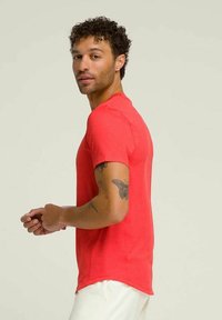 Camiseta roja de manga corta con cuello redondo, con un dobladillo ligeramente curvado y una textura suave. Exhibida en un modelo sobre un fondo neutro.