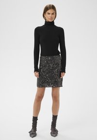 Fekete garbó felső, csillogó flitteres szoknyával párosítva. A szoknya szűk fazonú, különböző textúrákkal rendelkezik, és fekete lábbeli egészíti ki.