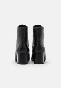 Botas de tobillo de cuero negro con una textura suave, tacón cilíndrico y parte superior redondeada con un corte alto en el tobillo.