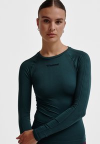 Mouwloze sporttop van teal stof, met een aansluitend ontwerp, geribbelde hals en textuurdetails langs de mouwen. Logo zichtbaar.