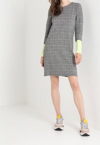 Grå rutiga klänning med långa ärmar som har neongröna manschetter. Kombinerad med beige och grå sneakers med gula detaljer.