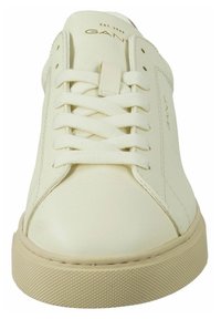 Weißer Ledersneaker mit abgerundeter Spitze, flachen Schnürsenkeln und einer strukturierten braunen Gummisohle. Mit geprägt sichtbarem Markenlogo und minimalen Designdetails.