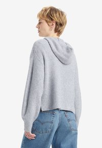 Gray ribbed knit hoodie with a relaxed fit and a spacious hood, paired with light blue denim jeans featuring back pocket detailing.