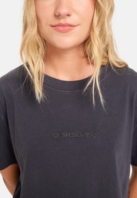 Mørkegrå bomulds t-shirt med korte ærmer, prydet med en tonet broderet "Quiksilver" logo på brystet. Glat overflade, rund halsudskæring.