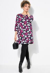 Bloemrijke tuniek met driekwartmouwen in zwart, wit en roze; voorzien van een keyhole-halslijn en gecombineerd met zwarte leggings en enkellaarzen.