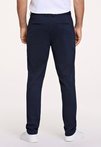 Pantaloni blu navy in tessuto morbido, con design a gamba dritta e tasche posteriori. Indossati con scarpe da ginnastica bianche e una t-shirt semplice.