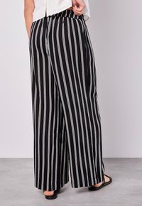 Black and white striped wide-leg pants with an elastic waistband and subtle texture, shown from the back, paired with black sandals.