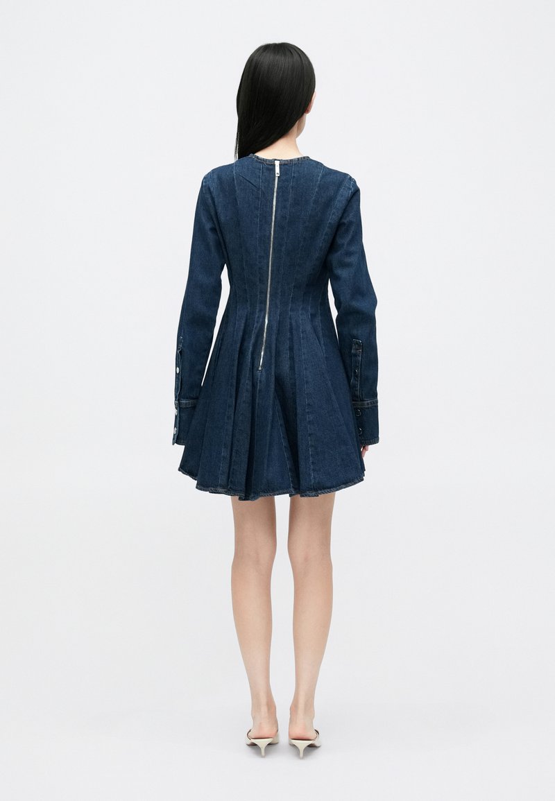 Robe en denim avec un corsage ajusté et une jupe évasée, dotée d'une fermeture éclair au dos et de manches longues avec des accents de boutons. Couleur bleu foncé.