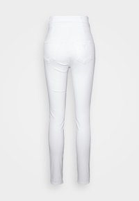 Valkoiset korkeavyötäröiset skinny-farkut, joissa on sileä rakenne, kahdet takataskut ja pieni kolmionmuotoinen emblem vyötärönauhassa.