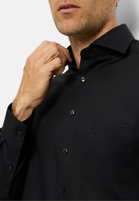 Camicia nera con bottoni, realizzata in tessuto morbido, colletto alla francese, taschino anteriore e delicato dettaglio del logo. Presenta bottoni scuri e una vestibilità sartoriale.