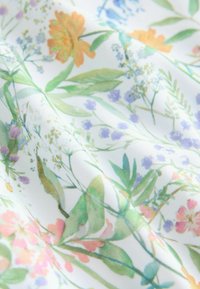 Tela con estampado floral que presenta vibrantes flores naranjas, rosas y moradas con hojas verdes sobre un fondo blanco, de textura suave y ligera.