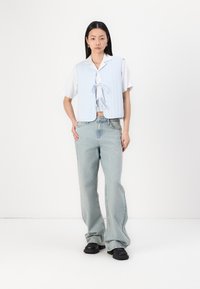 Lysblå quiltet vest med frontknytinger over en hvit skjorte, kombinert med lyse denim bell-bottom bukser og svarte platå sko.
