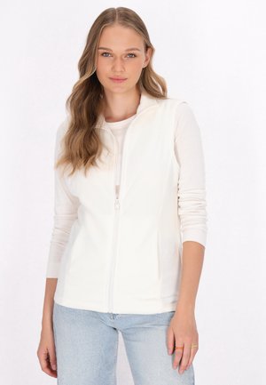 Gilet bianco con zip e tasche, realizzato in tessuto morbido. Indossato sopra una maglietta leggera, abbinato a jeans azzurri. Texture liscia, design minimale.