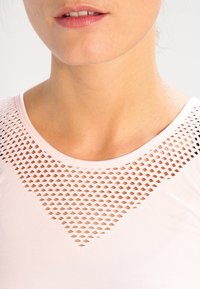 Ljusrosa topp med ett strukturerat nätkrage, med en triangulär utskärning. Mjuk tyg med normal passform och korta ärmar.