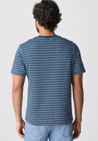 Camiseta de manga corta a rayas en tonos de azul y blanco. Tejido suave con cuello redondo y un corte relajado. Llevada con jeans de mezclilla claros.