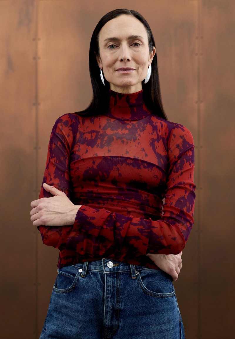 Haut à col roulé transparent à motifs rouges et violets, associé à un jean taille haute en denim. Des boucles d'oreilles en argent simples complètent la tenue.