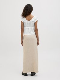 Witte katoenen blouse met gerimpelde mouwen, gecombineerd met een beige, enkellange rok van gestructureerde stof en zwarte schoenen met dikke zolen.