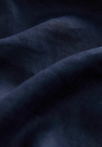 Donker marineblauw linnen stof, met een zachte textuur, subtiele geweven patronen en lichte kreukels, die het licht in verschillende tinten weerkaatst.