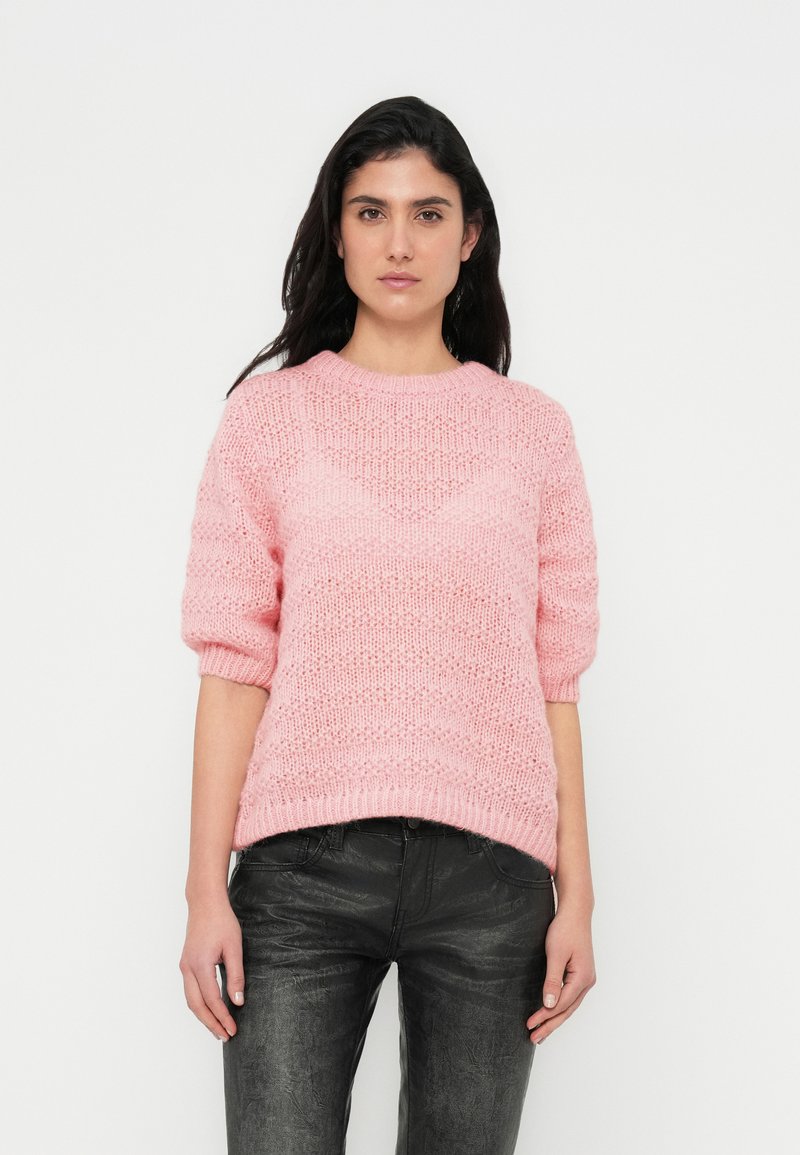 Ροζ πλεκτό πουλόβερ με κοντά μανίκια, με υφασμένο σχέδιο και ριμπ τελείωμα. Συνδυάζεται με μαύρο υφασμένο παντελόνι.