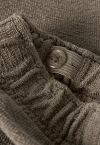 Gros plan sur un tissu brun texturé avec un bouton transparent à quatre trous fixé à une sangle élastique réglable.