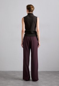 Donkerbruine mouwloze top gecombineerd met wijde paarse broeken. Zachte stof met een relaxte pasvorm; minimalistisch ontwerp, geen zichtbare patronen of hardware.