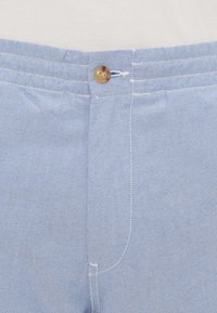 Pantaloni de culoare albastru deschis, cu un material texturat, închidere cu nasture și cusături contrastante de culoare albă pe margini.