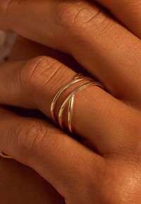 Trois anneaux en or entrelacés sur une main, présentant des surfaces lisses et polies, mettant en valeur leur design élégant et minimaliste.