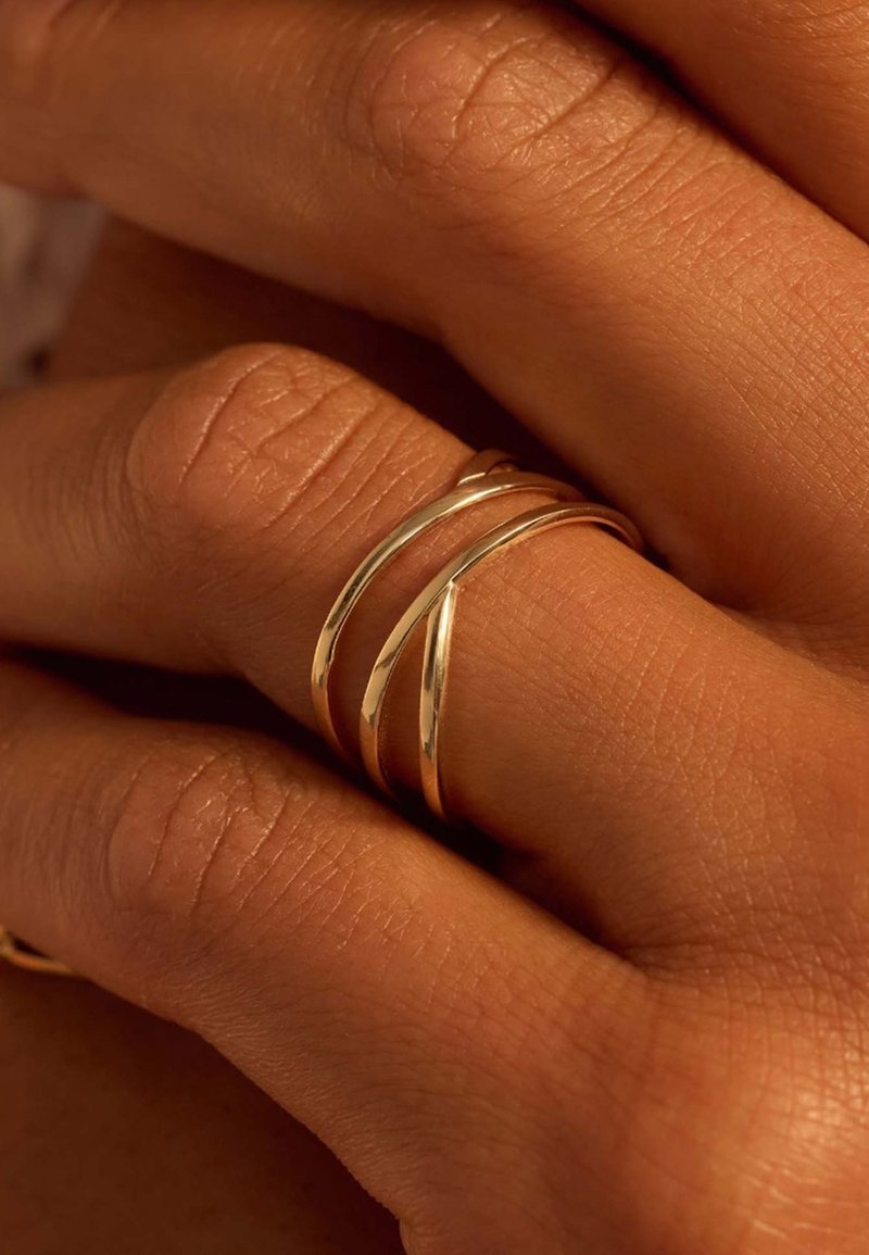 Trois anneaux en or entrelacés sur une main, présentant des surfaces lisses et polies, mettant en valeur leur design élégant et minimaliste.