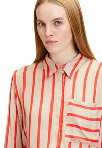 Beige button-up shirt with bold vertical red stripes, classic collar, and a pocket on the left chest with matching striping detail.