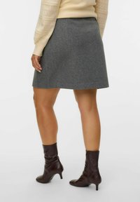 Jupe en laine grise au design évasé, avec une texture douce et un subtil détail de pli à l'arrière. Des bottes à talons marron complètent le look.