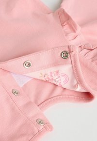 Rosa Baumwollkleidung mit Druckknopfverschluss, rundem Ausschnitt und Rüschendetails. Innentag zeigt Marke und Pflegeanweisungen.