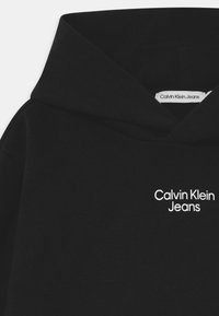 Sudadera con capucha negra de acabado texturizado, con el logo blanco "Calvin Klein Jeans" en el pecho. Cuenta con una capucha clásica con cordón ajustable.