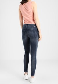 Jeans ajustados azules con una textura suave, cintura de altura media y dos bolsillos traseros. Combinados con una camiseta sin mangas rosa y zapatillas blancas.